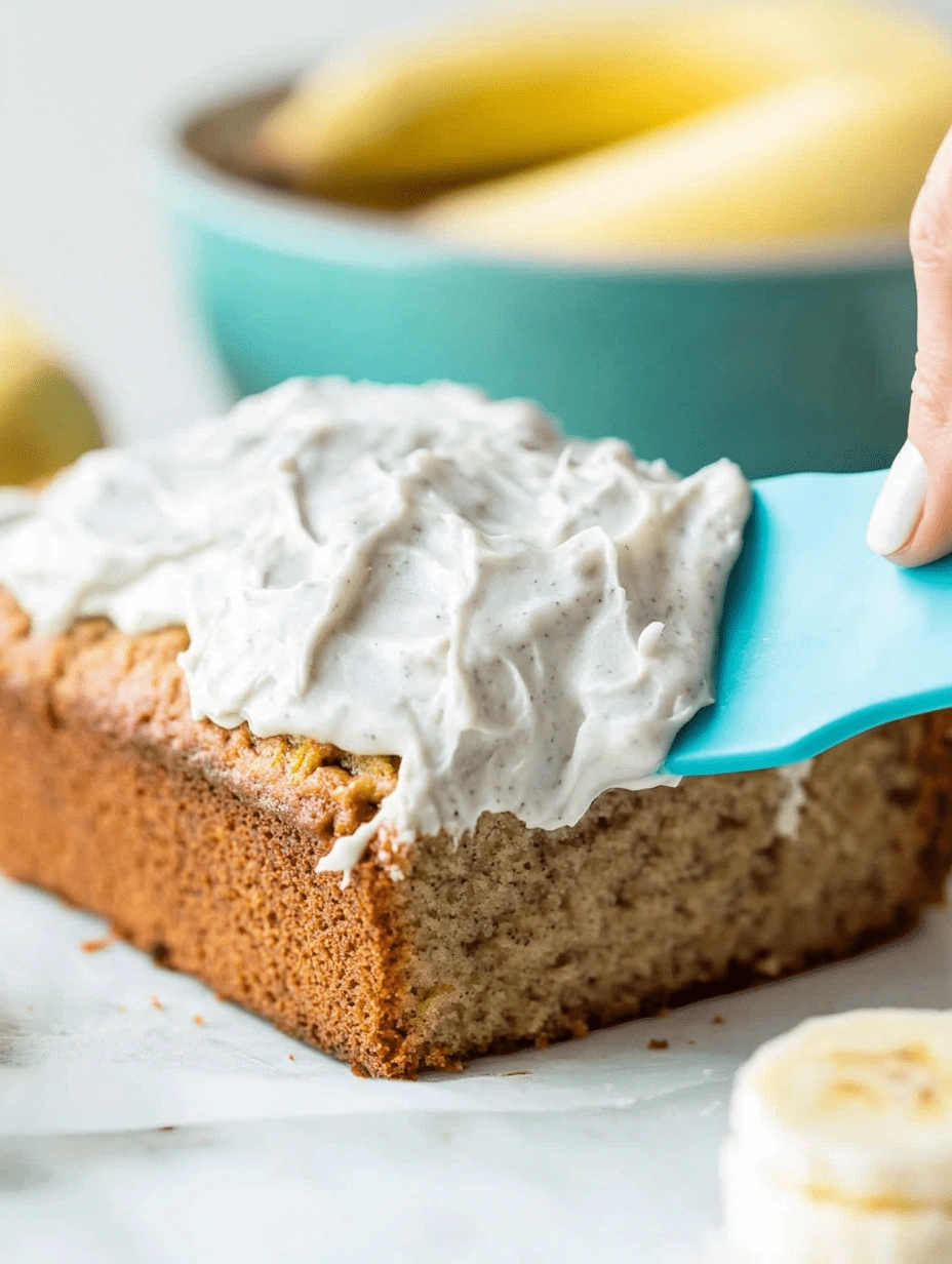 Spreading creamy frosting over a healthy banana cake loaf with a blue spatula